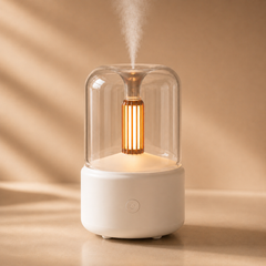 White diffuser with a warm amber glow and soft mist, shown on a neutral beige background.
